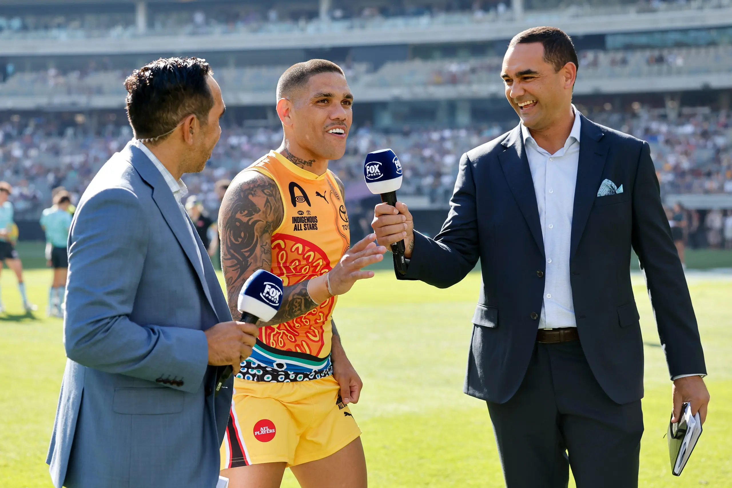 PERTH, AUSTRALIA - FEBRUARY 15: Michael Walters of the Indigenous All Stars is interviewed by Eddie Betts and Shaun Burgoyne during the 2025 Toyota AFL Indigenous All Stars match between the Indigenous All Stars and the Fremantle Dockers at Optus Stadium on February 15, 2025 in Perth, Australia. (Photo by Dylan Burns/AFL Photos via Getty Images)