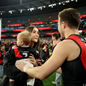 MELBOURNE, AUSTRALIA - AUGUST 21: Zach Merrett of the Bombers is congratulated by his wife Alexandra and son Jude during his 250th game the round 24 AFL match between Essendon Bombers and Carlton Blues at Melbourne Cricket Ground on August 21, 2025 in Melbourne, Australia. (Photo by Robert Cianflone/Getty Images)