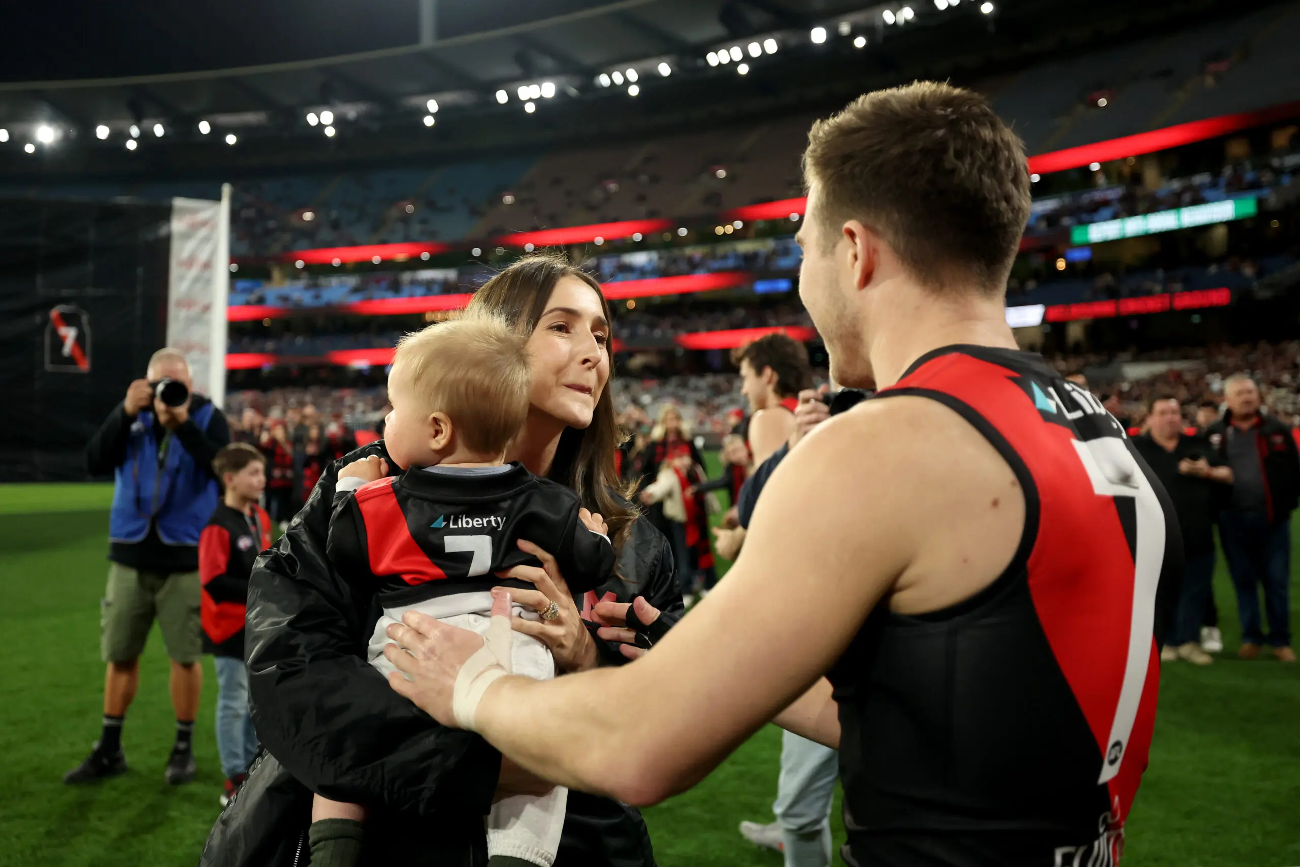 MELBOURNE, AUSTRALIA - AUGUST 21: Zach Merrett of the Bombers is congratulated by his wife Alexandra and son Jude during his 250th game the round 24 AFL match between Essendon Bombers and Carlton Blues at Melbourne Cricket Ground on August 21, 2025 in Melbourne, Australia. (Photo by Robert Cianflone/Getty Images)