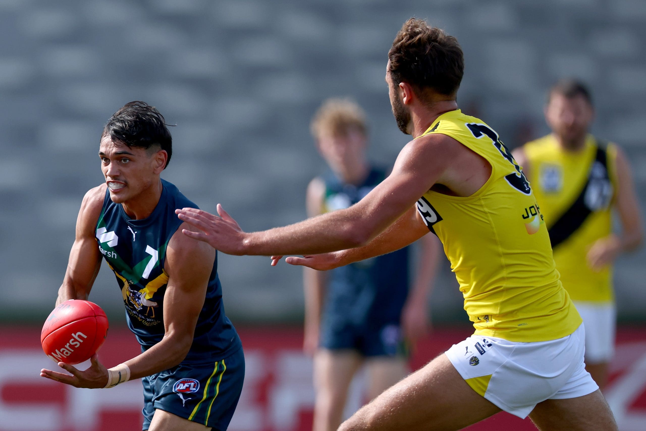 MELBOURNE, AUSTRALIA - APRIL 13: Dylan Patterson of the AFL National Academy handballs whilst being tackled by Mate Colina of the Tigers during the Marsh AFL National Academy Boys match between Australia U18 and Richmond VFL at RSEA Park on April 13, 2025 in Melbourne, Australia. (Photo by Josh Chadwick/AFL Photos/via Getty Images)