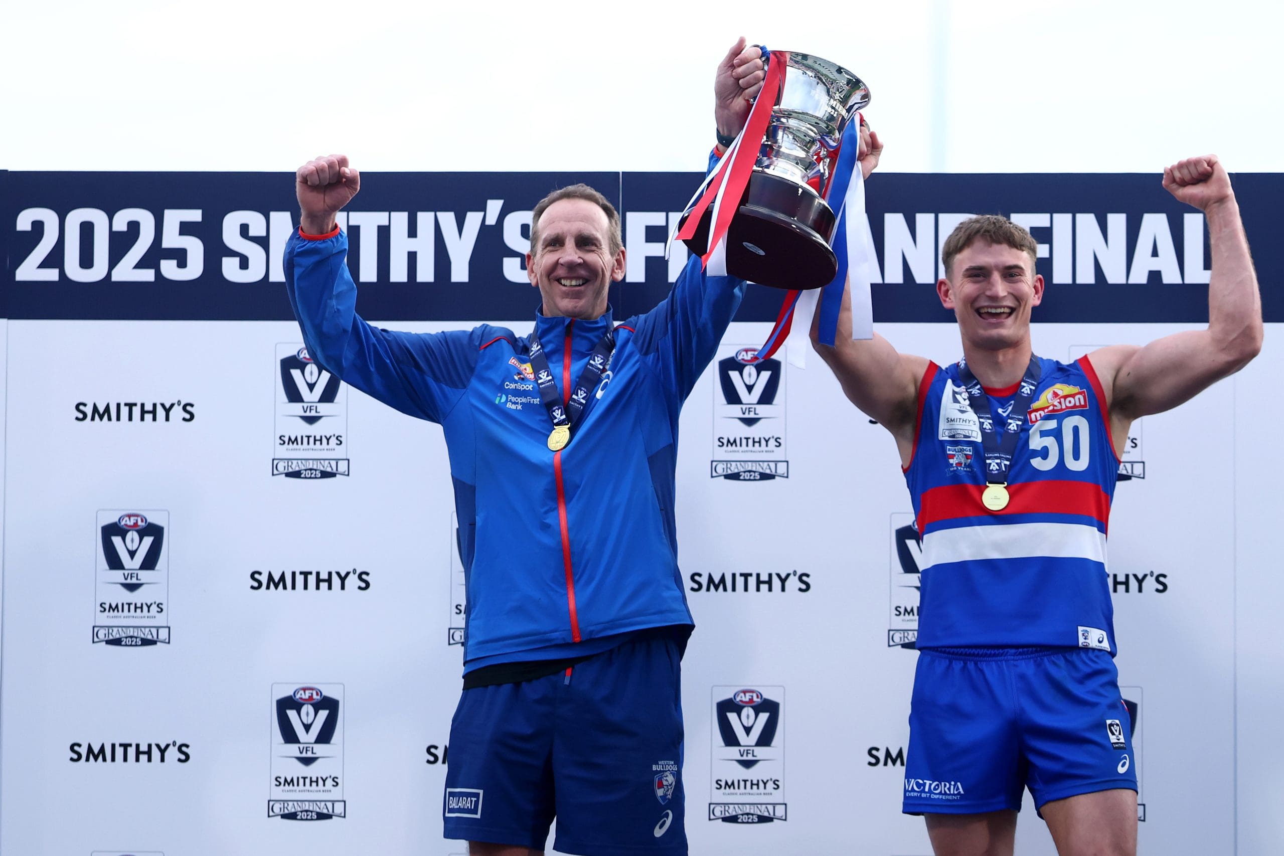 MELBOURNE, AUSTRALIA - SEPTEMBER 21: Stewart Edge, Senior Coach of the Bulldogs and Daniel Orgill of the Bulldogs hold the premiership cup aloft after winning the VFL Grand Final match between Footscray Bulldogs and Southport Sharks at Ikon Park on September 21, 2025 in Melbourne, Australia. (Photo by Josh Chadwick/AFL Photos/via Getty Images)